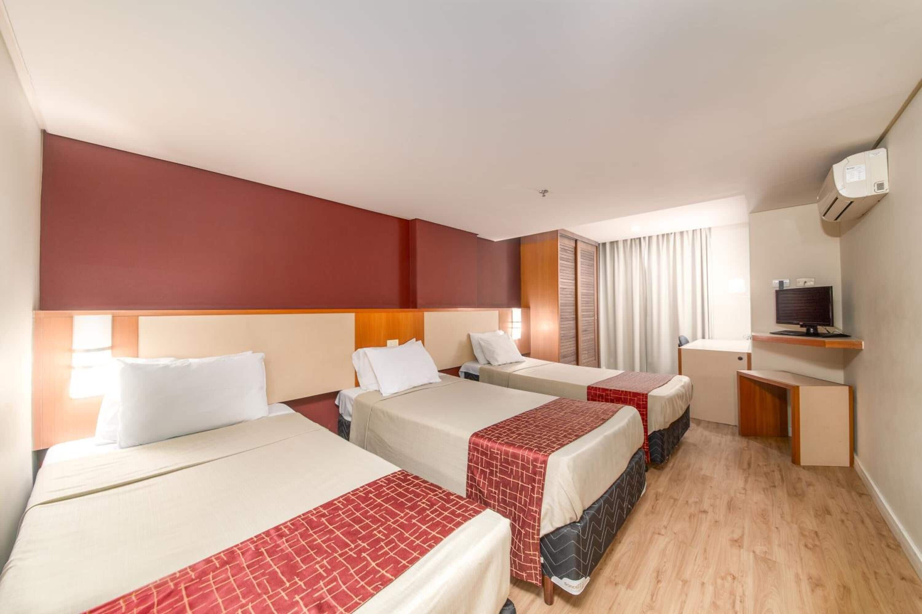 Quarto de hotel com três camas, uma mesa e uma televisão.