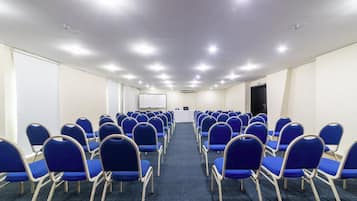 Uma sala de conferência com fileiras de cadeiras azuis, um quadro branco e um pódio.