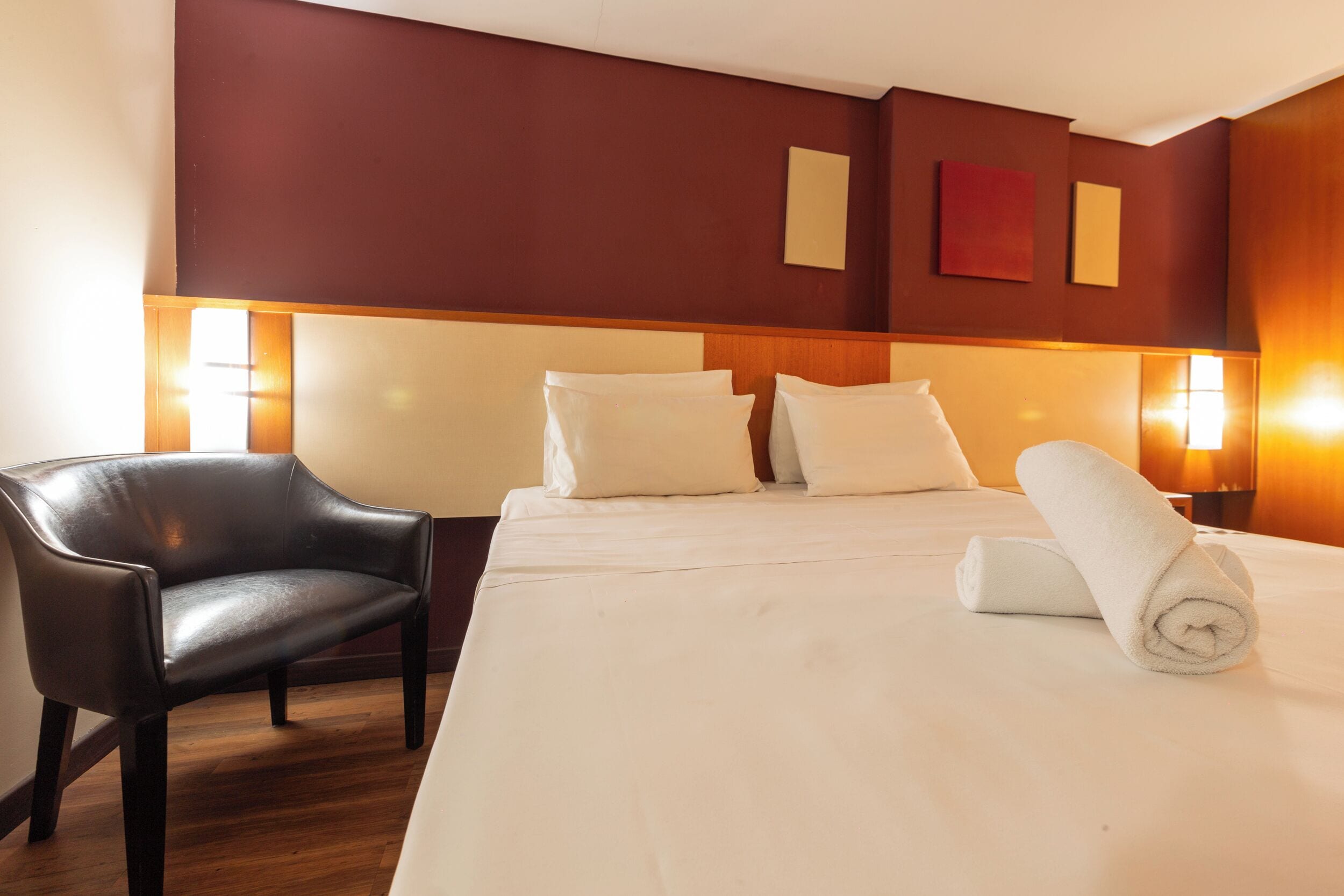 Quarto de hotel com uma cama grande, uma cadeira e duas luminárias fixadas na parede.