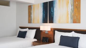 A hotel room with two beds, a wooden headboard, a nightstand with a lamp, and a large abstract painting on the wall.