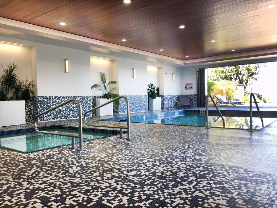 An indoor swimming pool with a tiled floor and walls, a metal ladder, and a 'No Diving' sign.