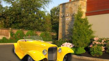 A yellow vintage car parked in front of a building with a stone facade and a sign that reads "GUILDFORD AM".