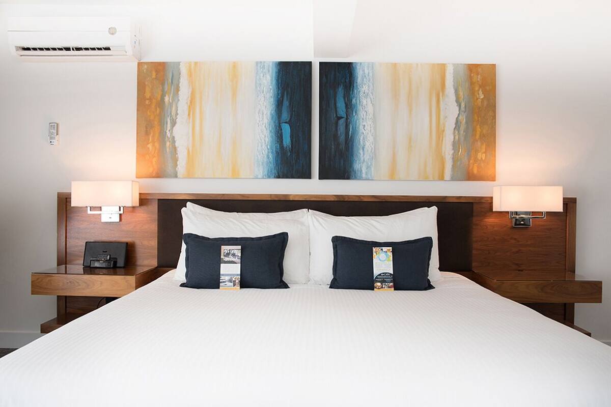 Una habitación de hotel con una cama grande, dos mesitas de noche y dos lámparas de pared.