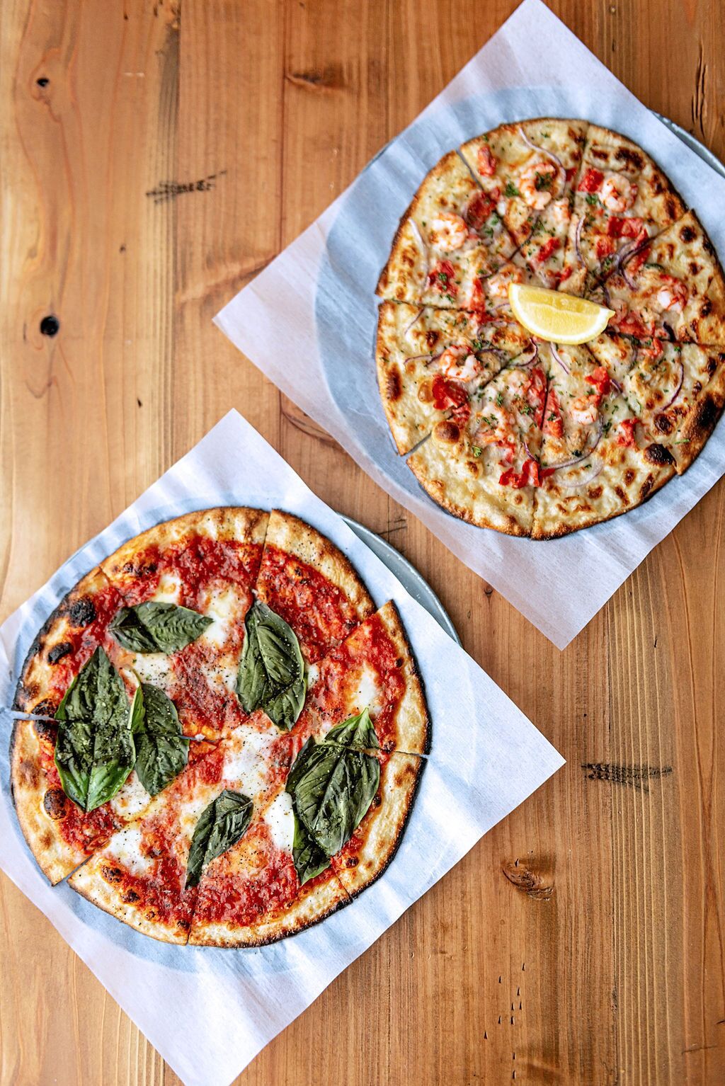 Two pizzas on wooden tables with pizza paper.