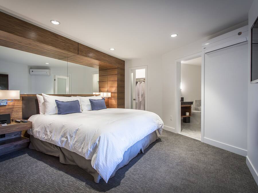 A modern hotel room with a large bed, a wooden accent wall, a flat-screen TV, and a walk-in closet.