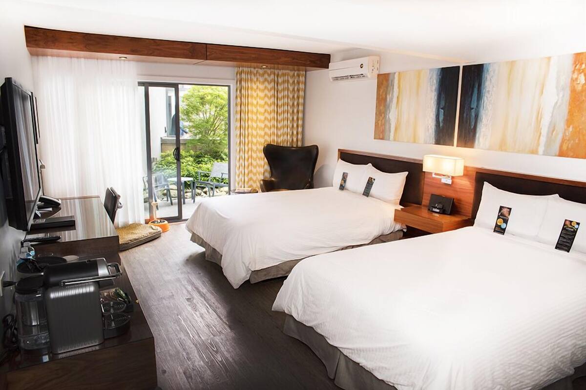 Habitación de hotel con dos camas, un escritorio con cafetera, televisión y puerta corrediza al exterior.