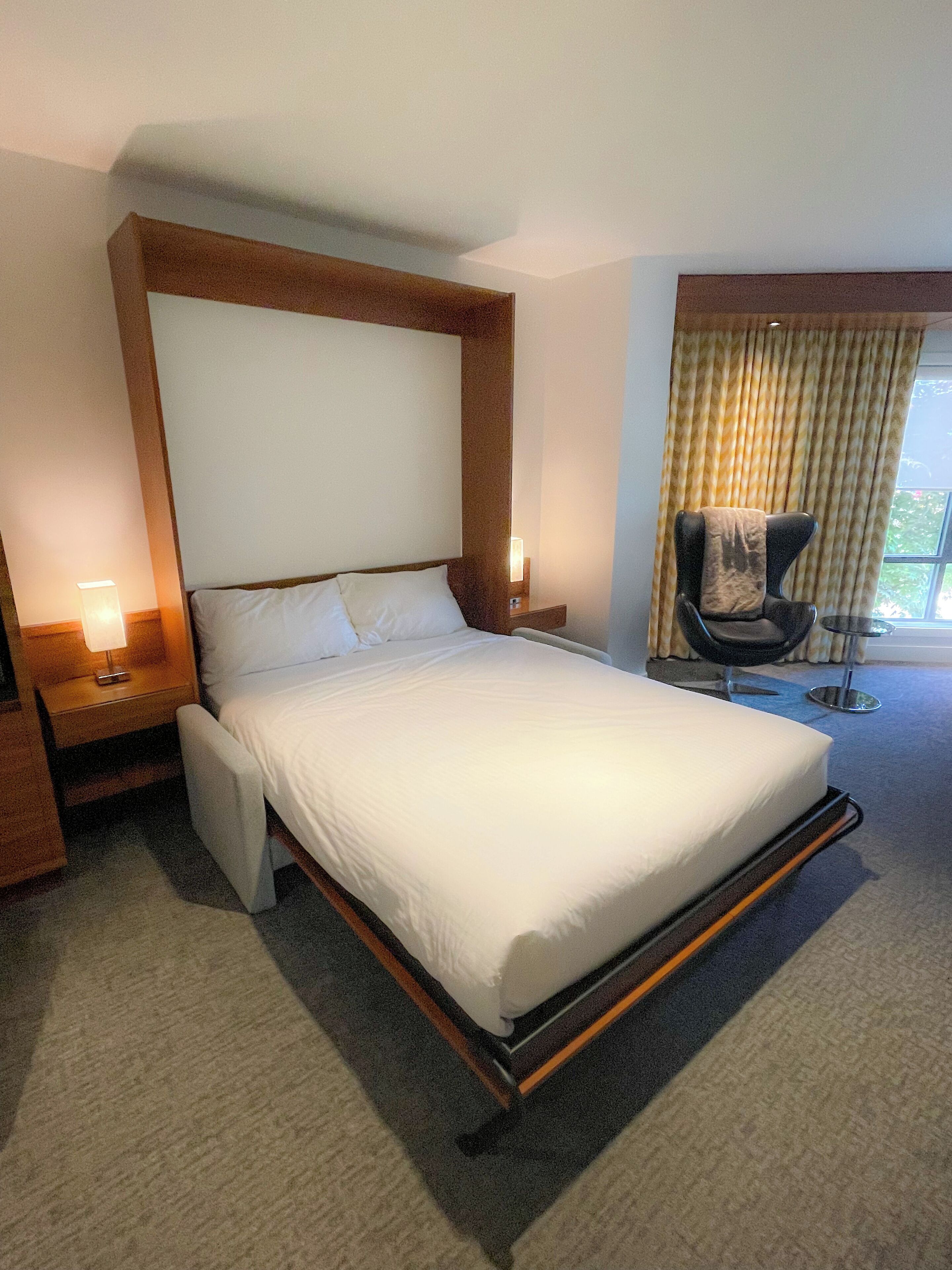 A hotel room with a large bed, a chair, a nightstand, and a window with curtains.