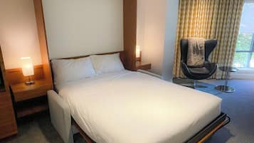 A hotel room with a large bed, a chair, a nightstand, and a window with curtains.