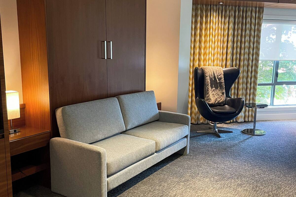 Una habitación moderna con sofá, una silla, armario y ventana con cortinas.