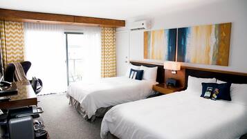 Ett hotellrum med två sängar, ett skrivbord med en stol och ett stort fönster med gardiner.