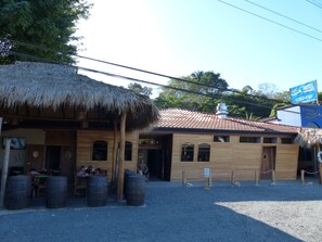 A wooden building with a thatched roof and a sign for a hotel. There are wooden barrels outside and a sign indicating a restaurant. - Costa Del Sol (Tárcoles)
