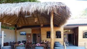 Un espacio de comedor al aire libre con mesas y sillas de madera, techo de paja y barriles de madera.