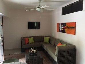A living room with a sectional sofa, a flat-screen TV, a ceiling fan, and a painting on the wall. - Costa Del Sol (Tárcoles)