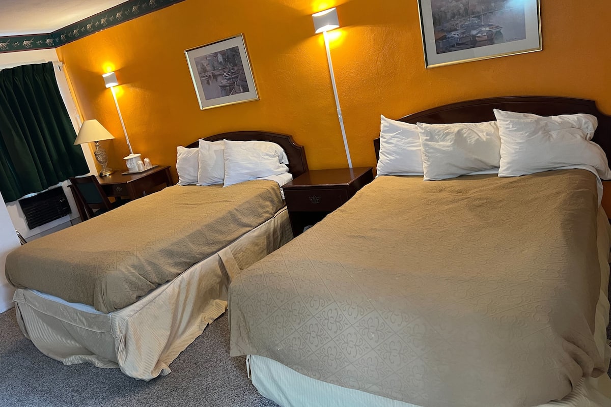 Una habitación de hotel con dos camas, una mesita de noche, una lámpara y un cuadro en la pared.
