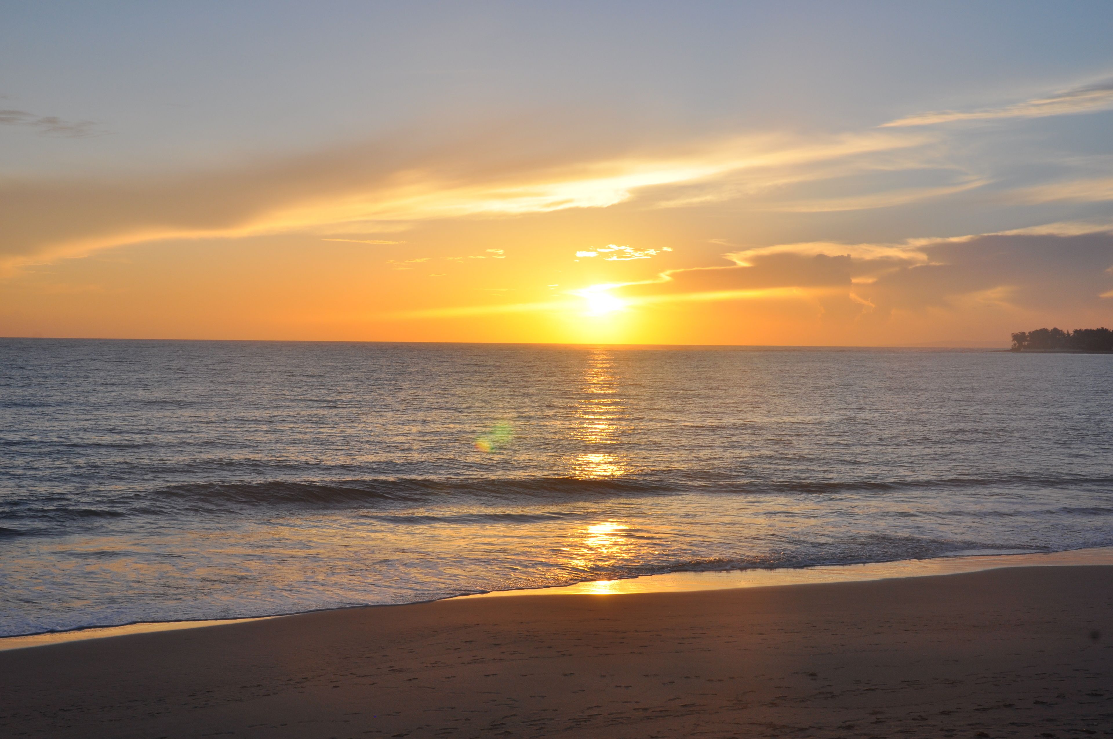 Una playa al atardecer, con el sol reflejado en el agua.
