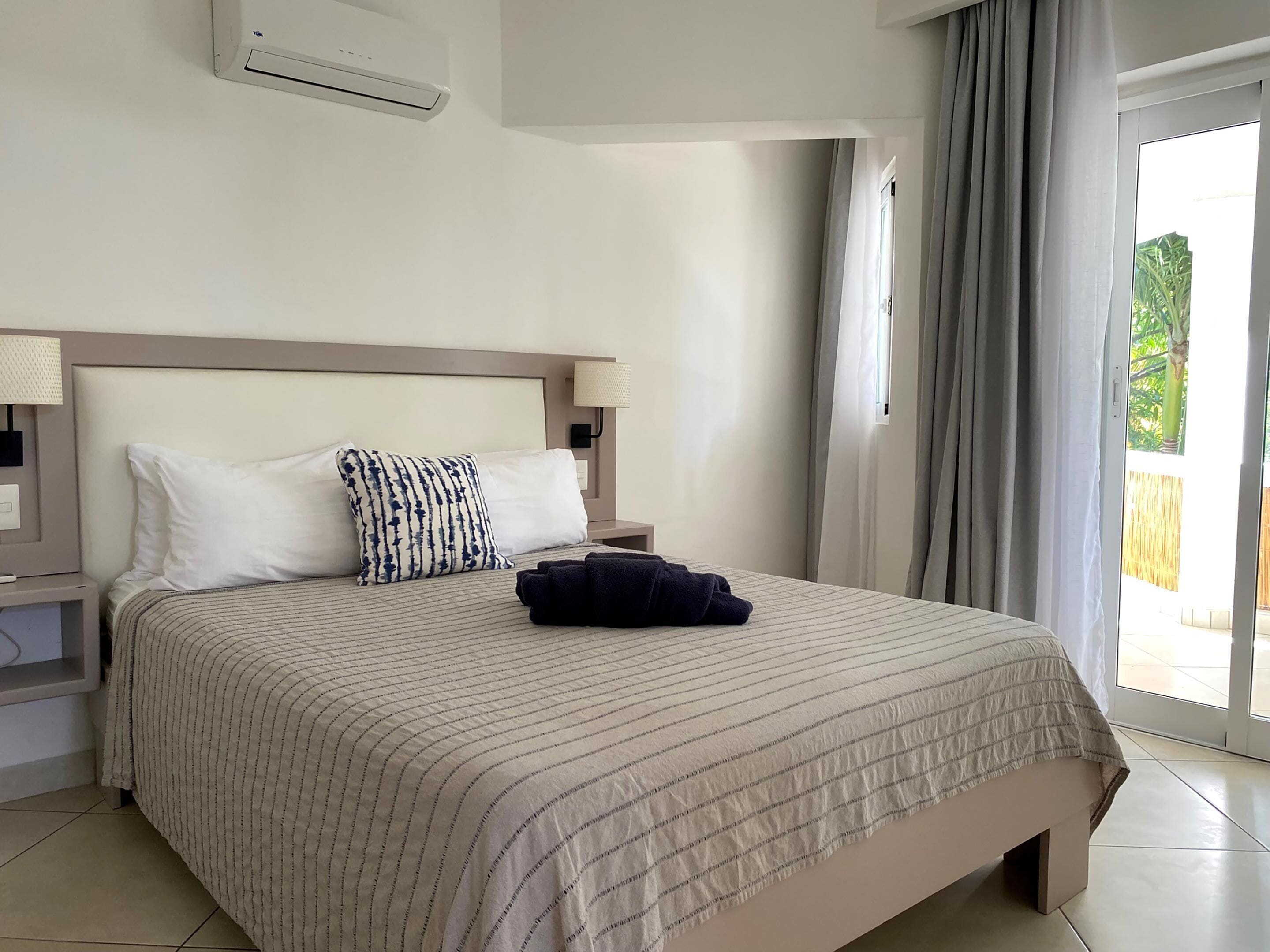 A hotel room with a bed, two bedside lamps, a window with curtains, and a view of the outdoors.