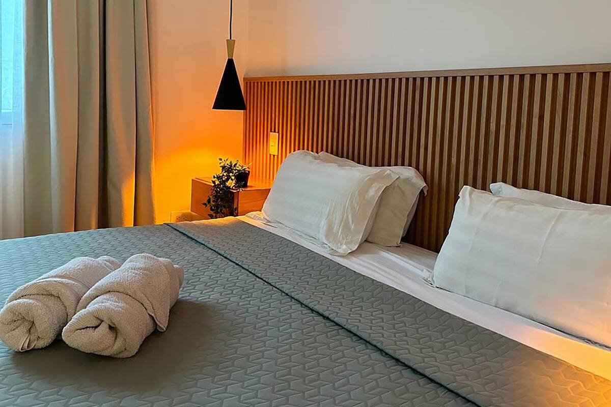 A hotel room with a bed, pillows, a bedside table with a lamp, and a window with curtains.