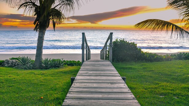 A wooden pathway leading to a beach with a sunset view.