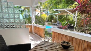 A wooden table with two wine glasses and a bowl, surrounded by wicker furniture and a bamboo wall.