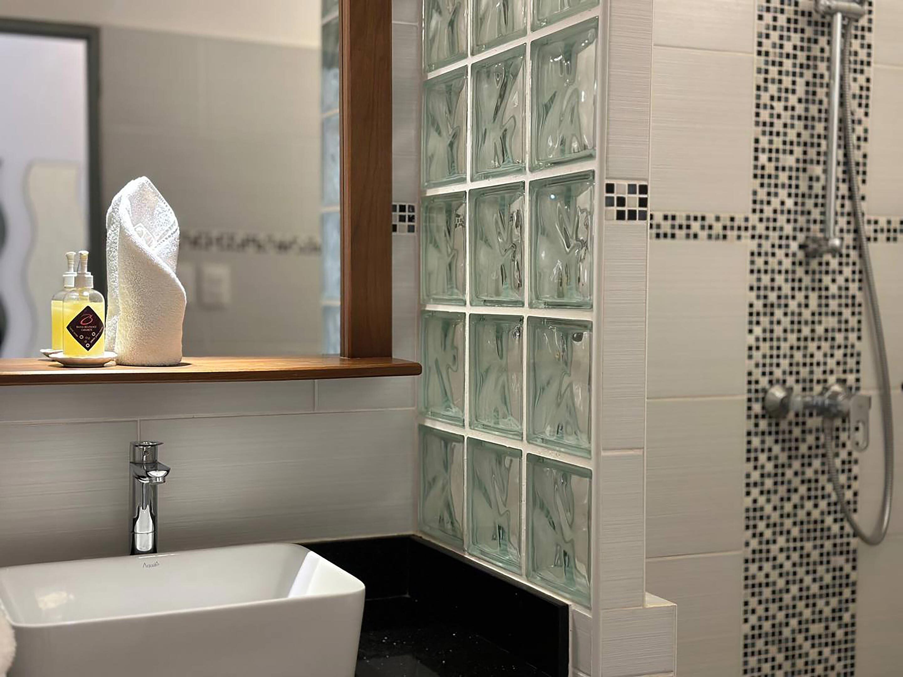 A bathroom with a white sink, a glass shower enclosure, and a tiled wall with a mosaic pattern.