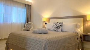 A hotel room with a large bed, a chair, a bedside table, and an air conditioning unit.