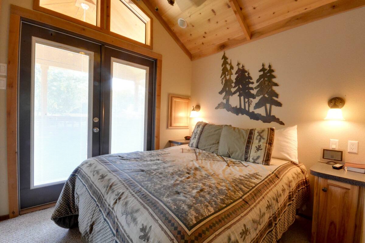 A bedroom with a large bed, a wooden ceiling, a wall-mounted lamp, and a door with glass panels.