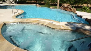 A swimming pool with a hot tub area, surrounded by a stone deck and a fence.