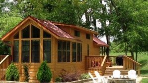 A wooden cabin with a porch, large windows, and a stone fireplace.