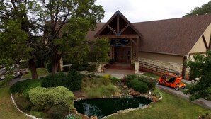 A lodge with a pond, surrounded by well-maintained landscaping and a vehicle parked nearby.