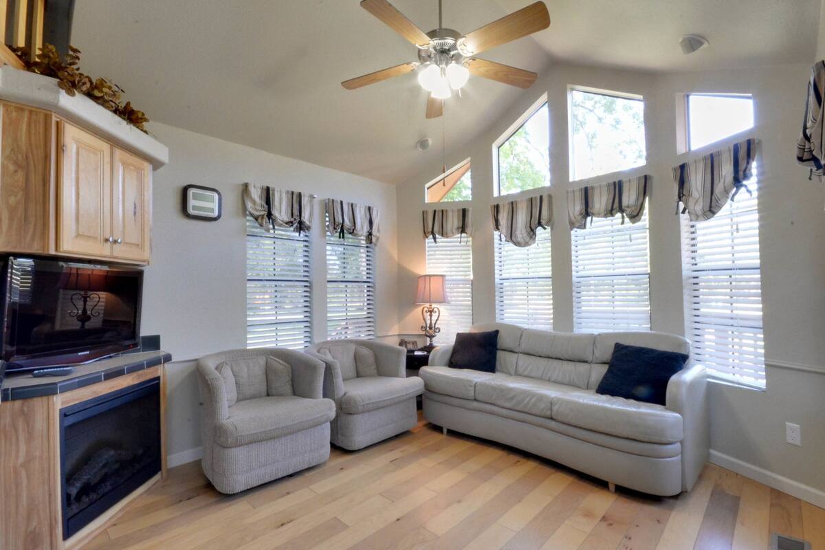 A living room with a fireplace, two armchairs, a sofa, and a ceiling fan.