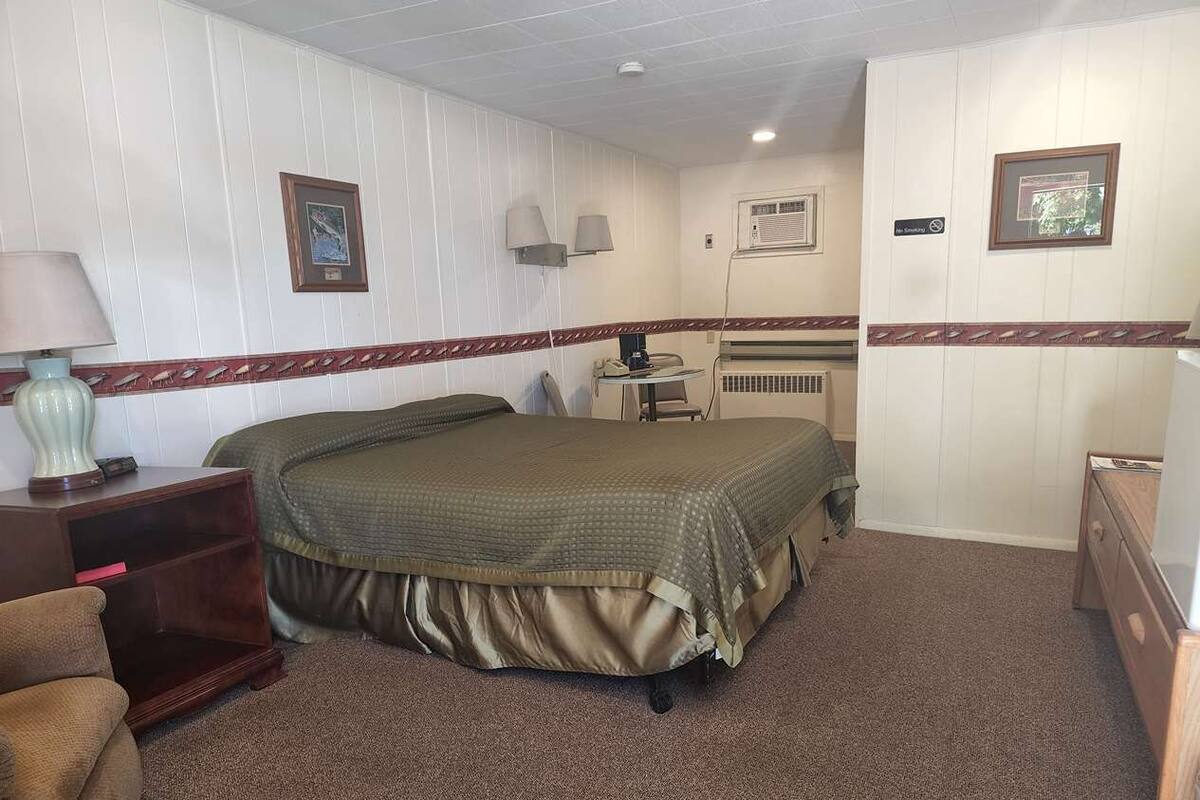 Ein Hotelzimmer mit Bett, Schreibtisch, Stuhl, Lampe und Kommode.