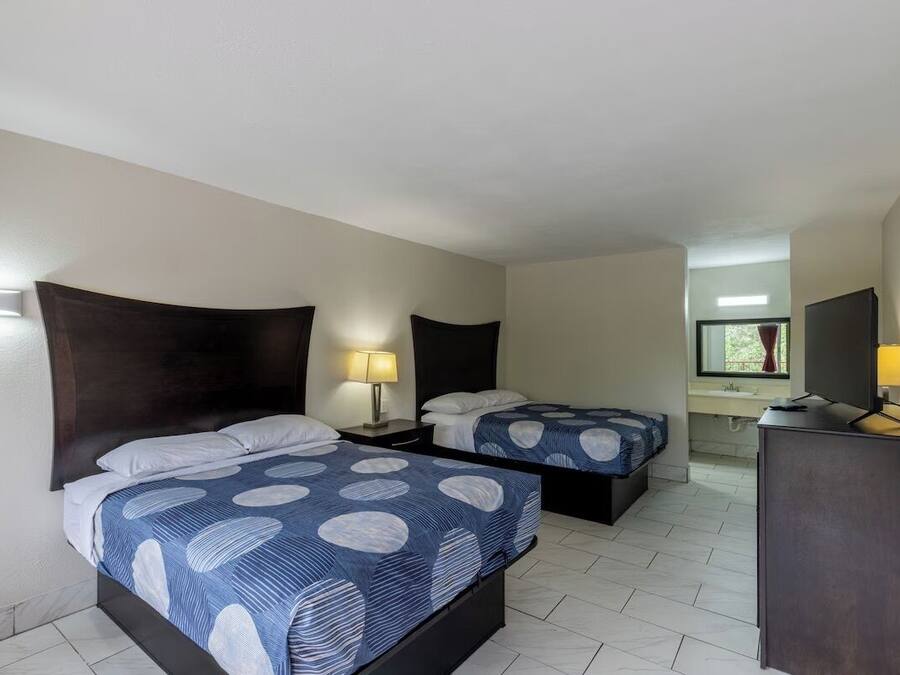 Habitación de hotel con dos camas, cada una con cabecero, mesitas de noche con lámparas, un escritorio y una ventana con vistas.