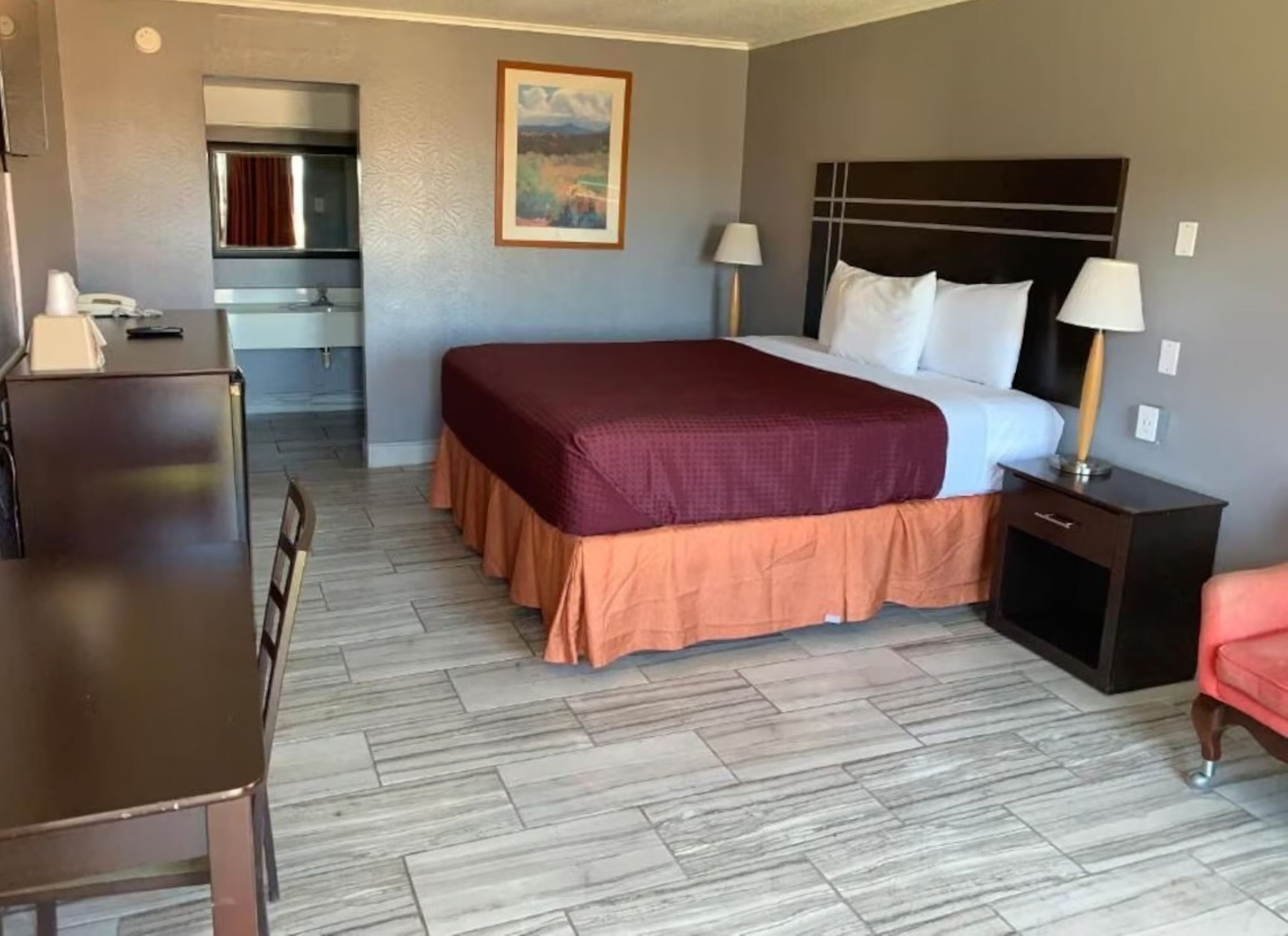 A hotel room with a bed, bedside tables, a desk, and a kitchenette.