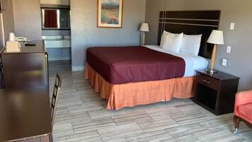 Quarto de hotel com cama, mesas de cabeceira, escrivaninha e cozinha compacta.