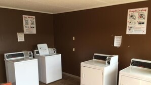 A laundry room with four white washers and dryers, brown walls, and informational posters on the walls.