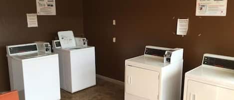 A laundry room with four white washers and dryers, brown walls, and informational posters on the walls.