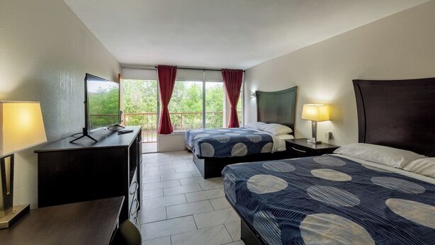 A hotel room with two beds, a desk, a chair, a TV, and a window with curtains.