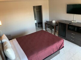 Una habitación de hotel con cama, escritorio, silla, televisor y armario.