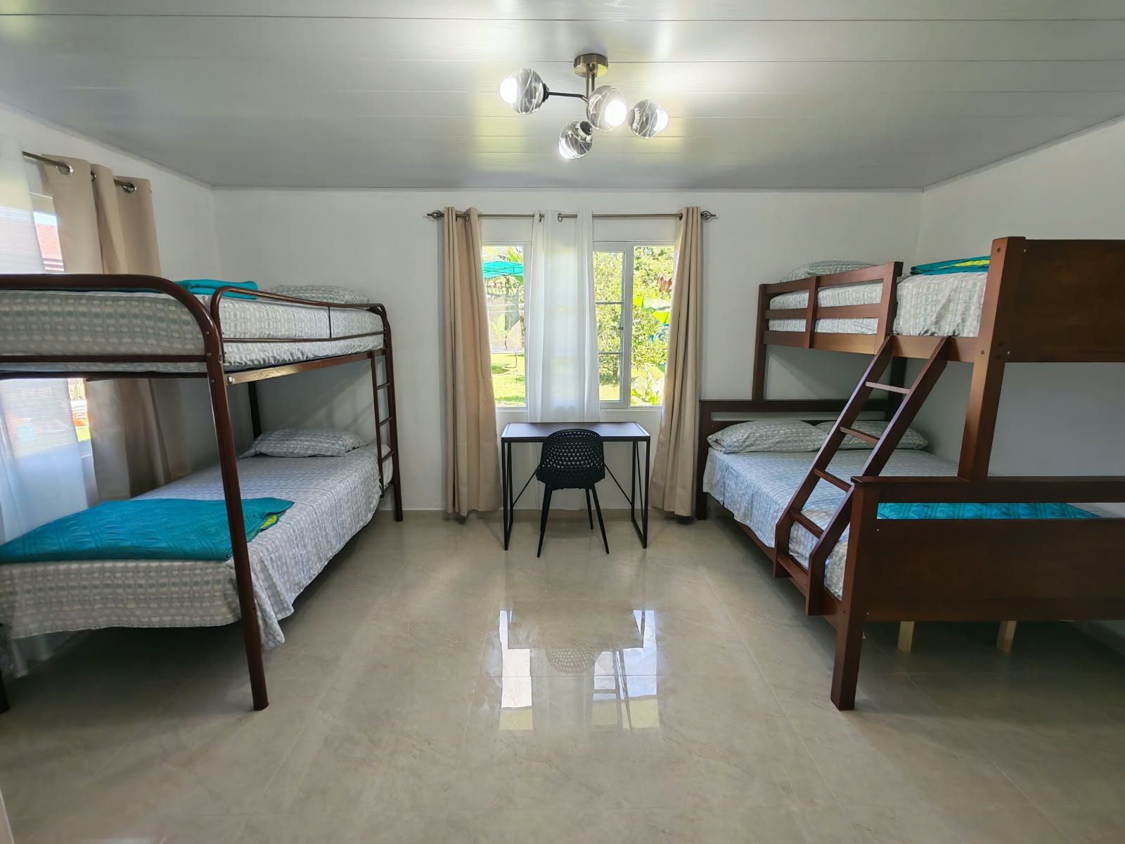 A dormitory room with bunk beds, a small desk, and a window with curtains.