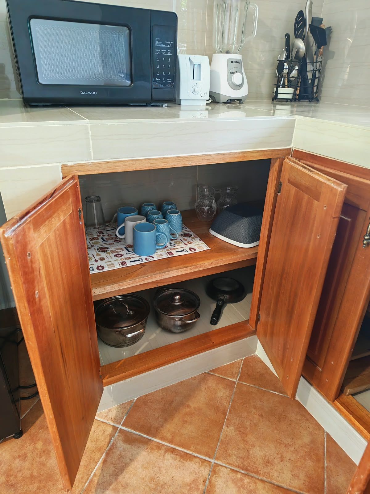 A kitchen with a microwave, toaster, and a shelf with mugs and cookware.