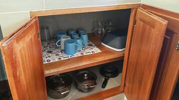 A kitchen with a microwave, toaster, and a shelf with mugs and cookware.