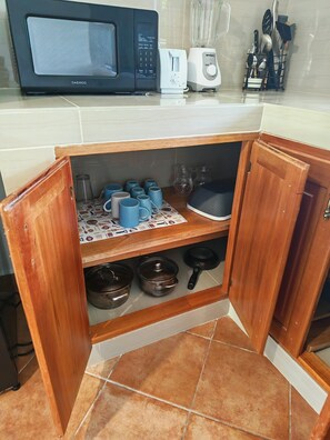 Una cocina con microondas, tostadora y una estantería con tazas y utensilios de cocina.
