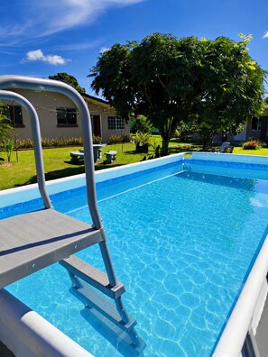 A swimming pool with a metal ladder, surrounded by a well-maintained lawn and a house in the background. - Little Italy B&B (Tijeras)