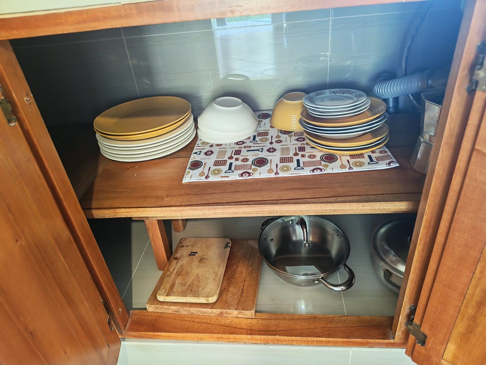 A kitchen cabinet with stacked plates, bowls, and a cutting board.