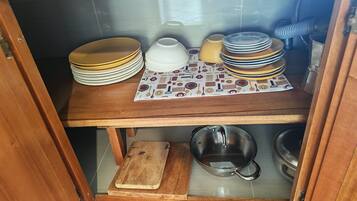 A kitchen cabinet with stacked plates, bowls, and a cutting board.