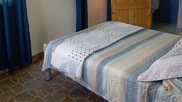 A bedroom with a bed, a TV mounted on the wall, a wooden door, and a bathroom with a tiled wall and sink.