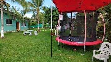 A trampoline under a red canopy in a grassy backyard with palm trees and a house in the background.