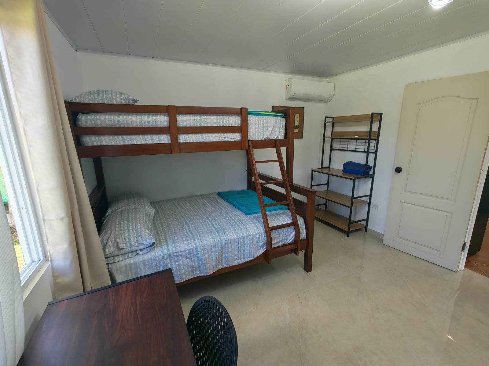 A bunk bed room with a desk and a chair, a shelf unit, and an air conditioning unit on the wall.