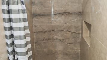 A shower area with a striped shower curtain, a window, and a marble wall.