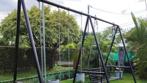 A swing set with two swings, surrounded by a grassy area and a chain-link fence. - Little Italy B&B (Tijeras)